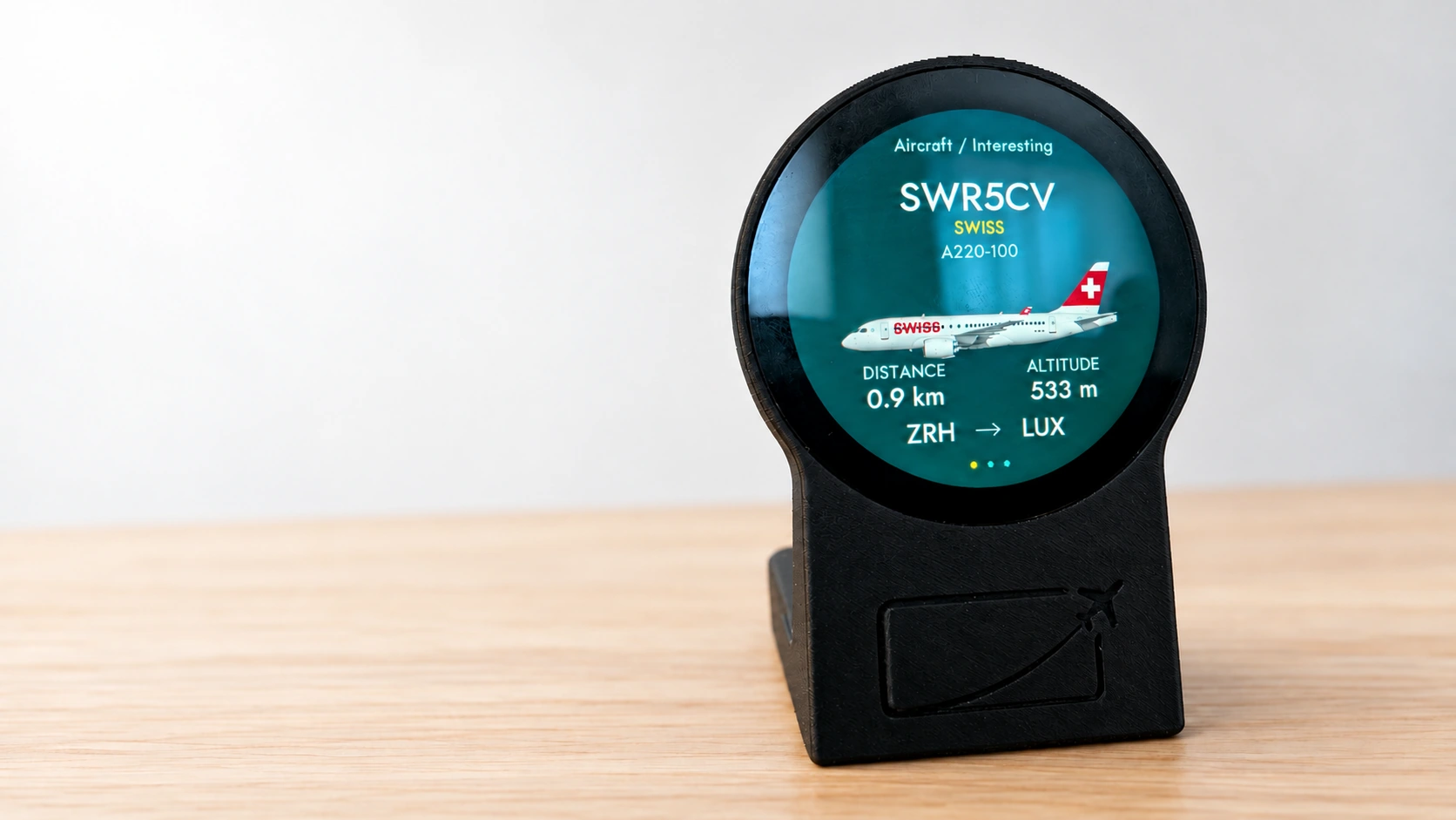 PlaneSlate Micro in a black printed desk housing on a wooden desk, displaying a SWISS flight
